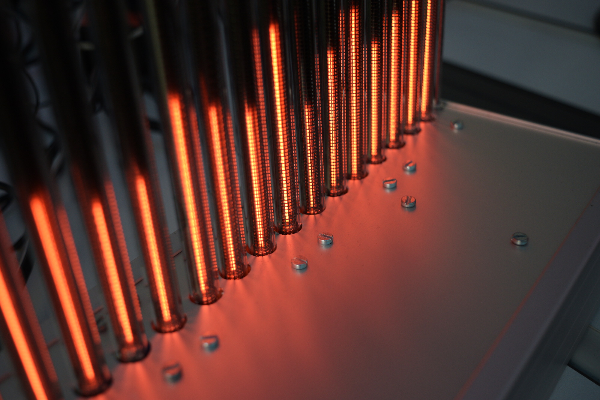 An aluminium case with several bargraph nixie tubes protruding from it. The orange-red glow of the tubes is reflected in the aluminium surface of the case